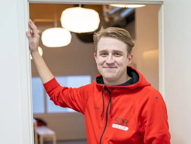 mies nojaa oven karmiin punainen huppari yllään ja hymyilee