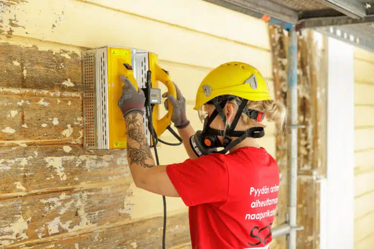 Maalari poistaa lämmittimellä maalia kirkon seinästä.