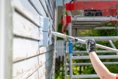 Kuvassa leveä pensseli jatkovarella maalaa talon seinää