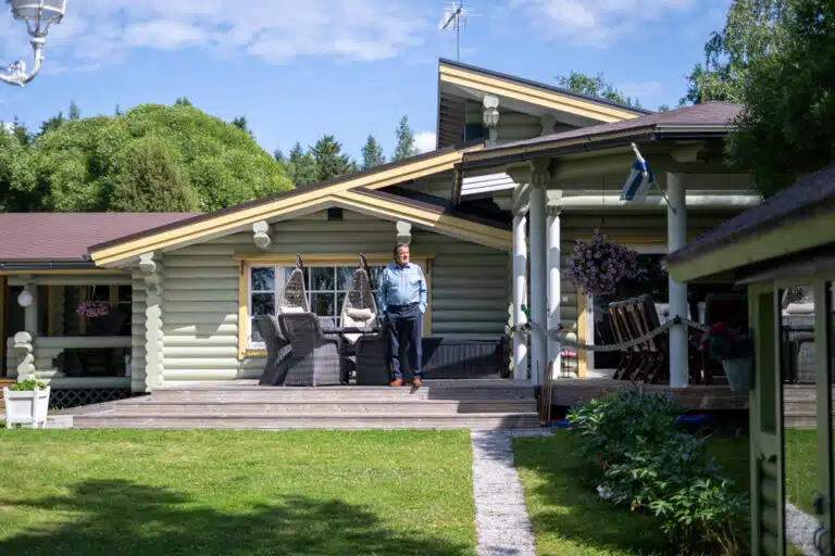 Tyytyväinen mies seisoskelee juuri maalatun hirsihuvilan portailla