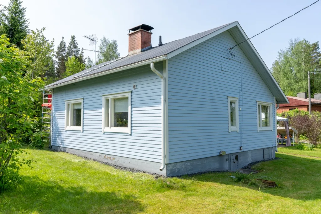 Sivinen pieni puutalo kesäisessä maisemassa