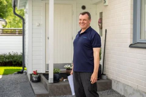 Mies seisoo asuntonta edustalla hymyille leveästi.