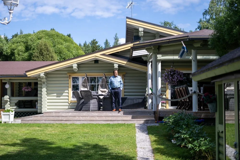 Tyytyväinen mies seisoskelee juuri maalatun hirsihuvilan portailla