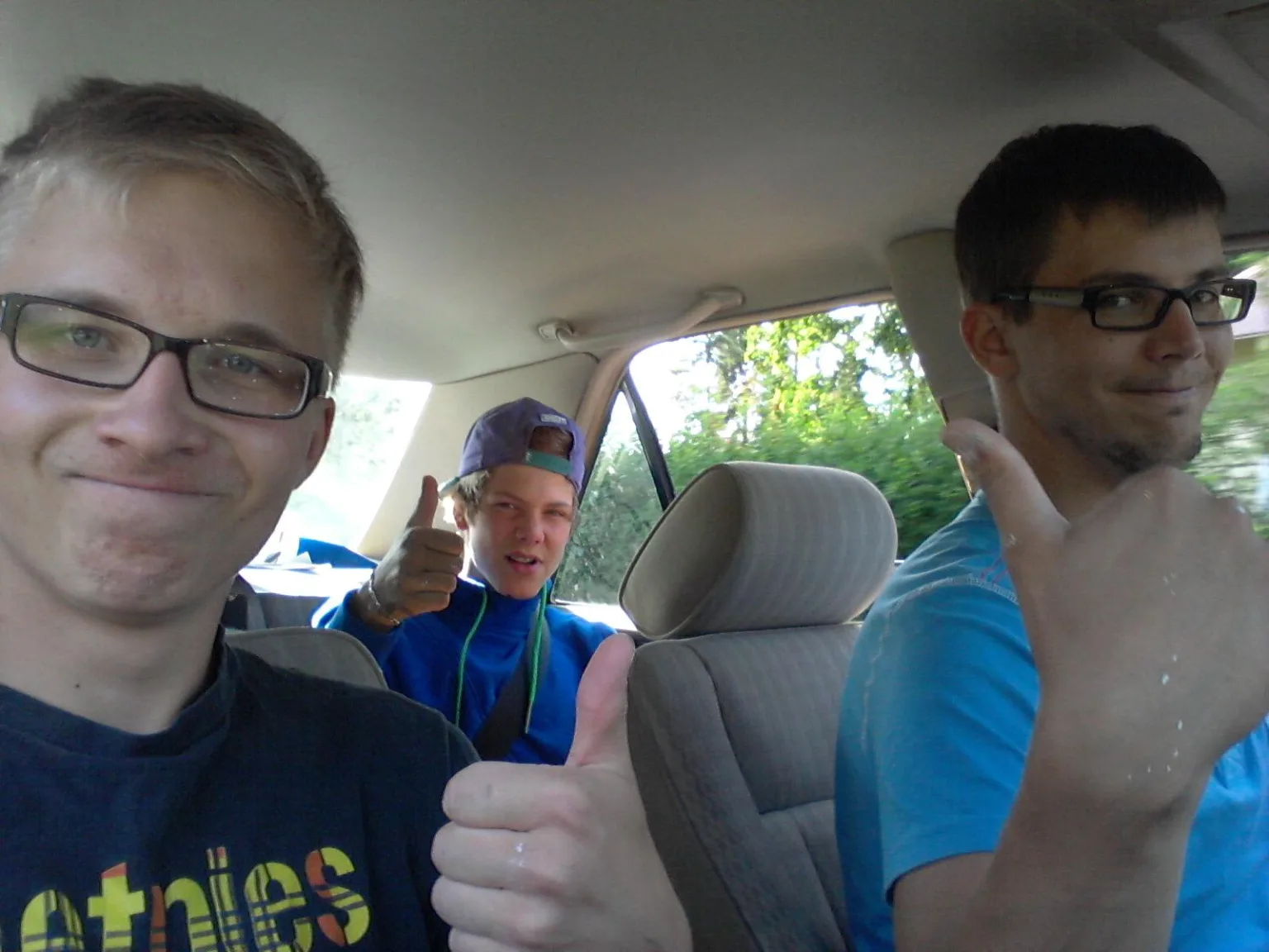 Kuvassa kolme nuorta miestä autossa näyttää peukkua.