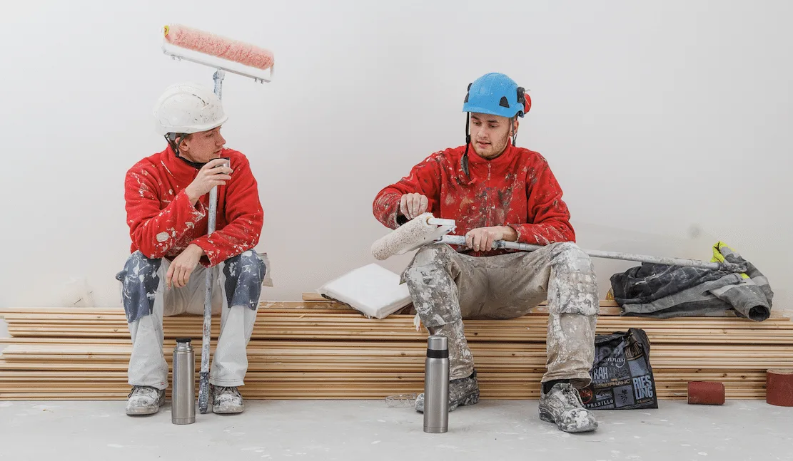 ||Maalari levittää telalla harmaata maalia betonilattialle punainen paita yllään