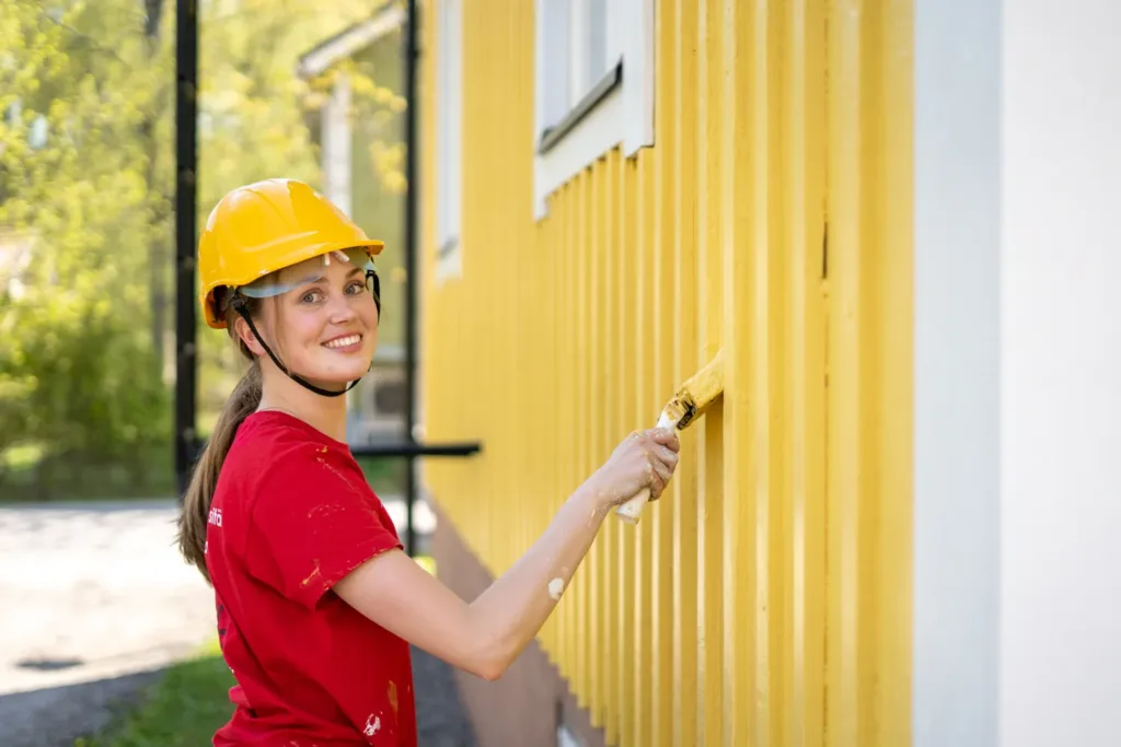 Sorcolorin talon ulkomaalaus maalari maalaamassa keltaista taloa