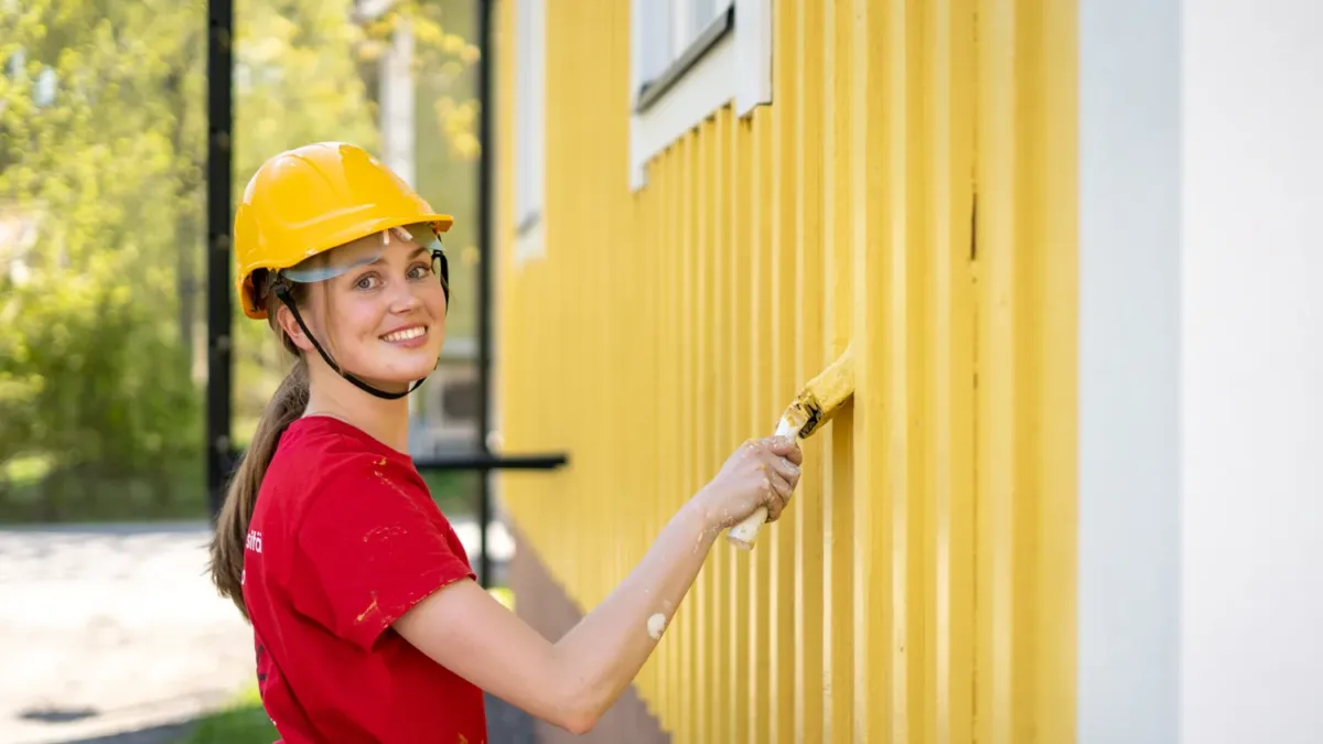 Sorcolorin talon ulkomaalaus maalari maalaamassa keltaista taloa