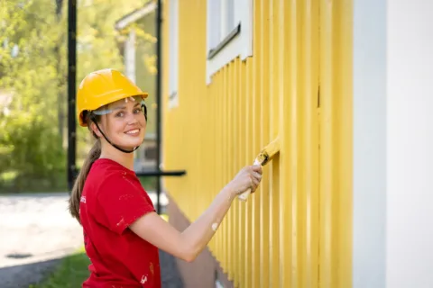 Sorcolorin talon ulkomaalaus maalari maalaamassa keltaista taloa